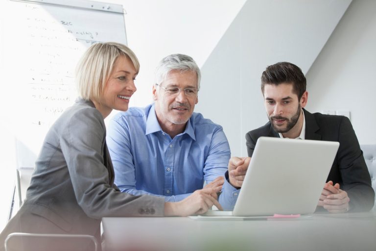 three people gathered on a desk, looking at a laptop smartly dressed.